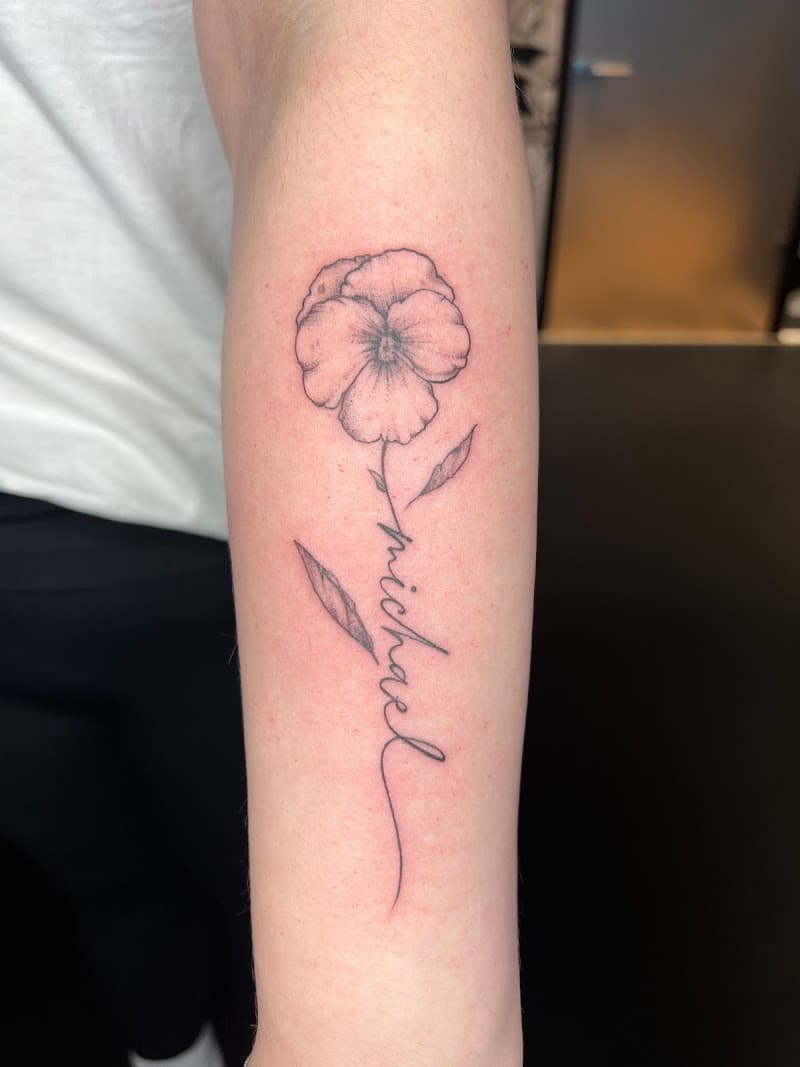 Fineline viooltje met de naam 'Michael' als steel op de onderarm.