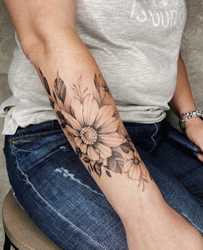 Zwart-wit bloementattoo met een grote madelief en bladeren op de onderarm.