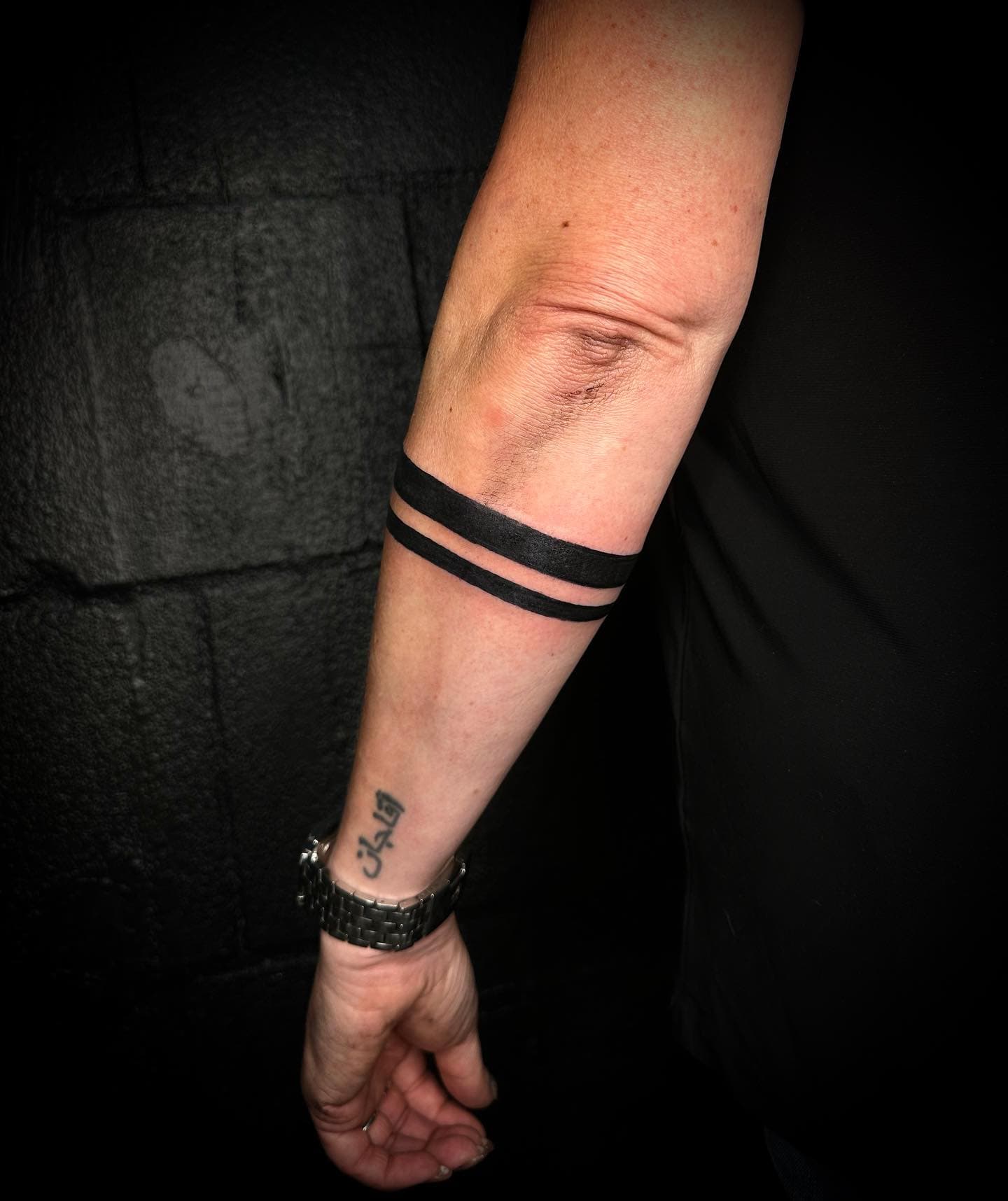 Twee strakke zwarte banden om de onderarm en een kleine tekst op de pols.