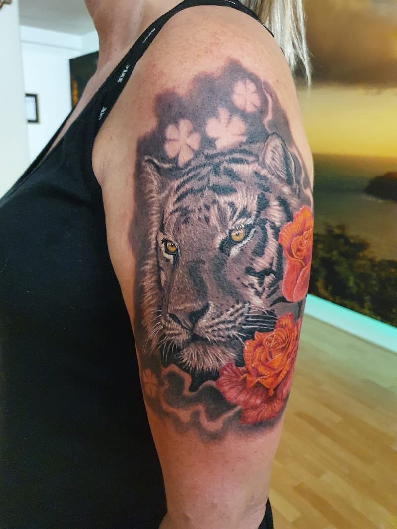 Realistische tijgerkop met oranje rozen en klavertjes op bovenarm.