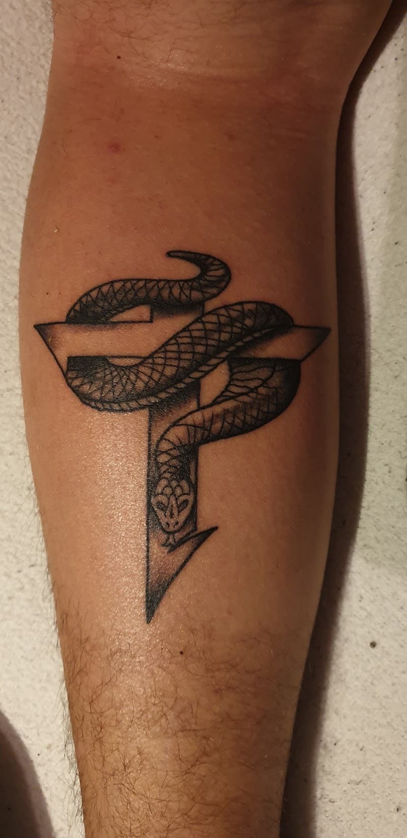 Zwart-wit tattoo van een slang gewikkeld om een gestileerde letter P op het onderbeen.