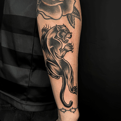 Zwart-witte traditionele panter tattoo op onderarm, met roos en prikkeldraad.