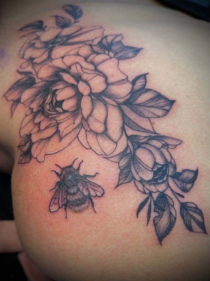 Zwart-wit tattoo van pioenrozen en een bij op de schouder.