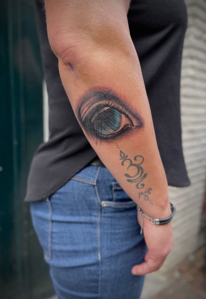 Realistisch oog met blauwe iris en Om-symbool op onderarm.