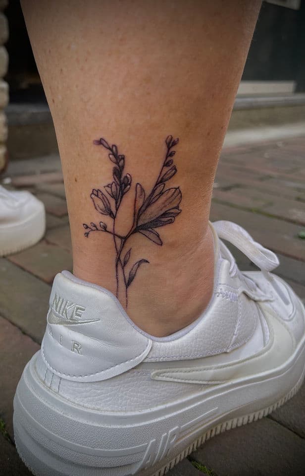 Fineline bloementak tattoo op de enkel.