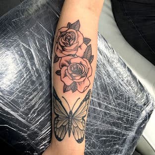 Zwart-wit tattoo van twee rozen en een vlinder op de onderarm.