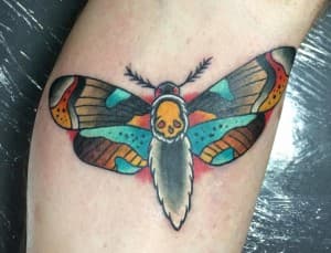 Traditional mot tattoo met doodshoofd op onderarm.