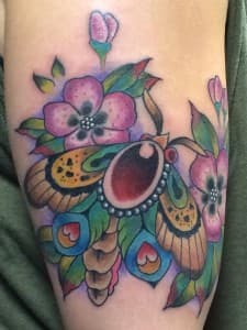 Kleurrijke neo-traditionele mot met bloemen op bovenarm.