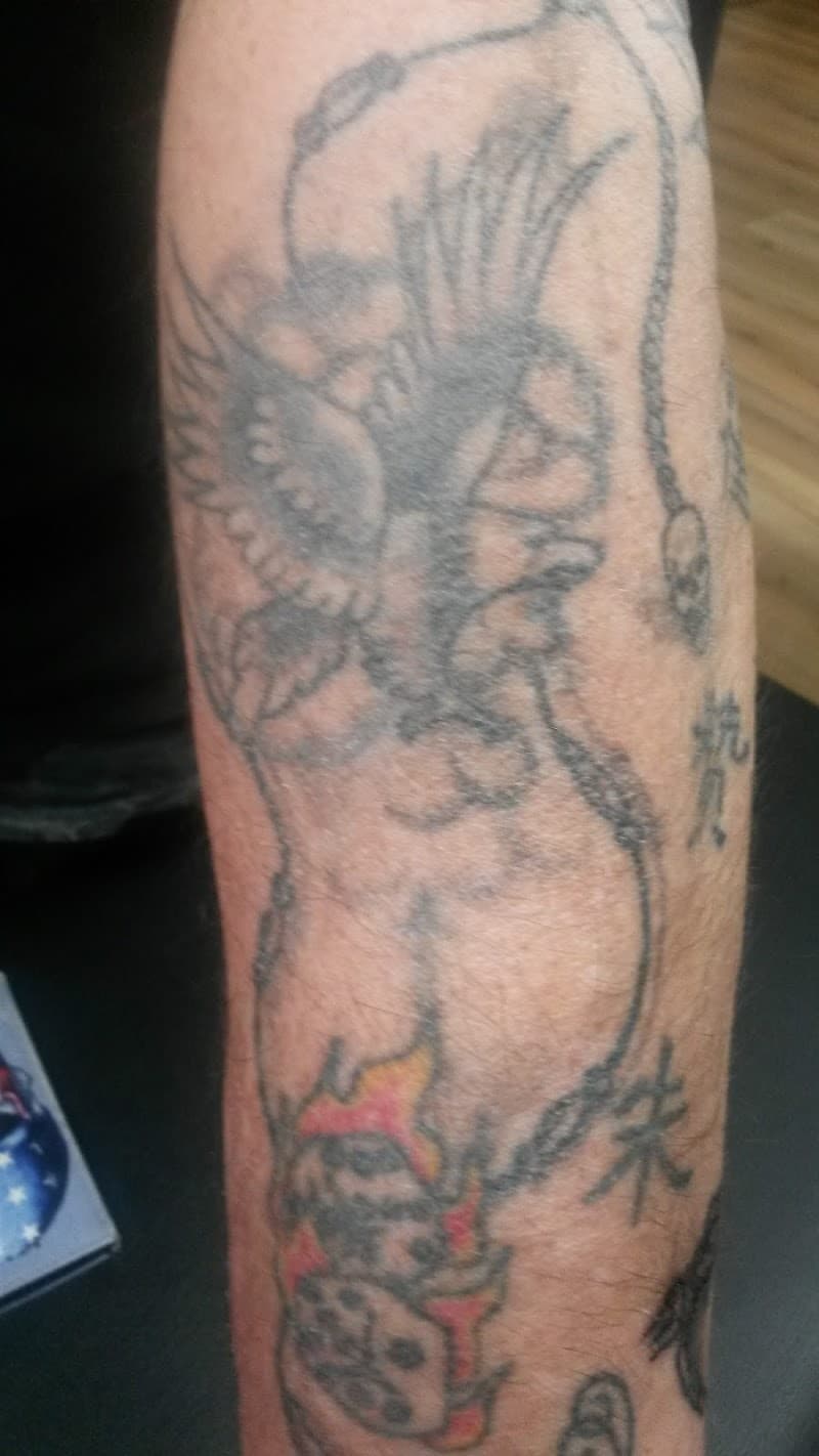 Oude, vervaagde tattoo van een gevleugelde figuur en een schedel met vlammen.