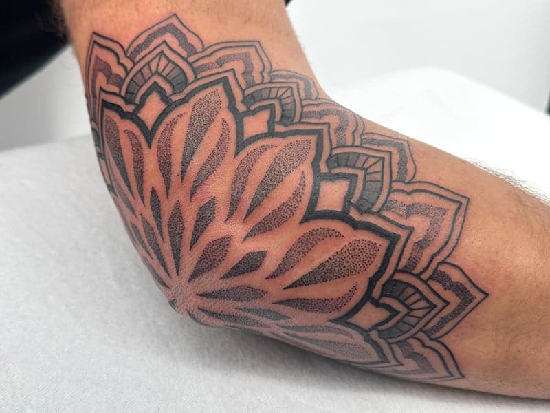 Grote mandala tattoo op de elleboog, gezet in dotwork en geometrische stijl.