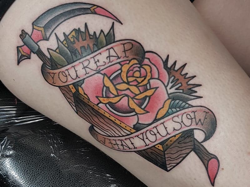 Traditional tattoo met zeis, roos en 'You Reap What You Sow' banner.