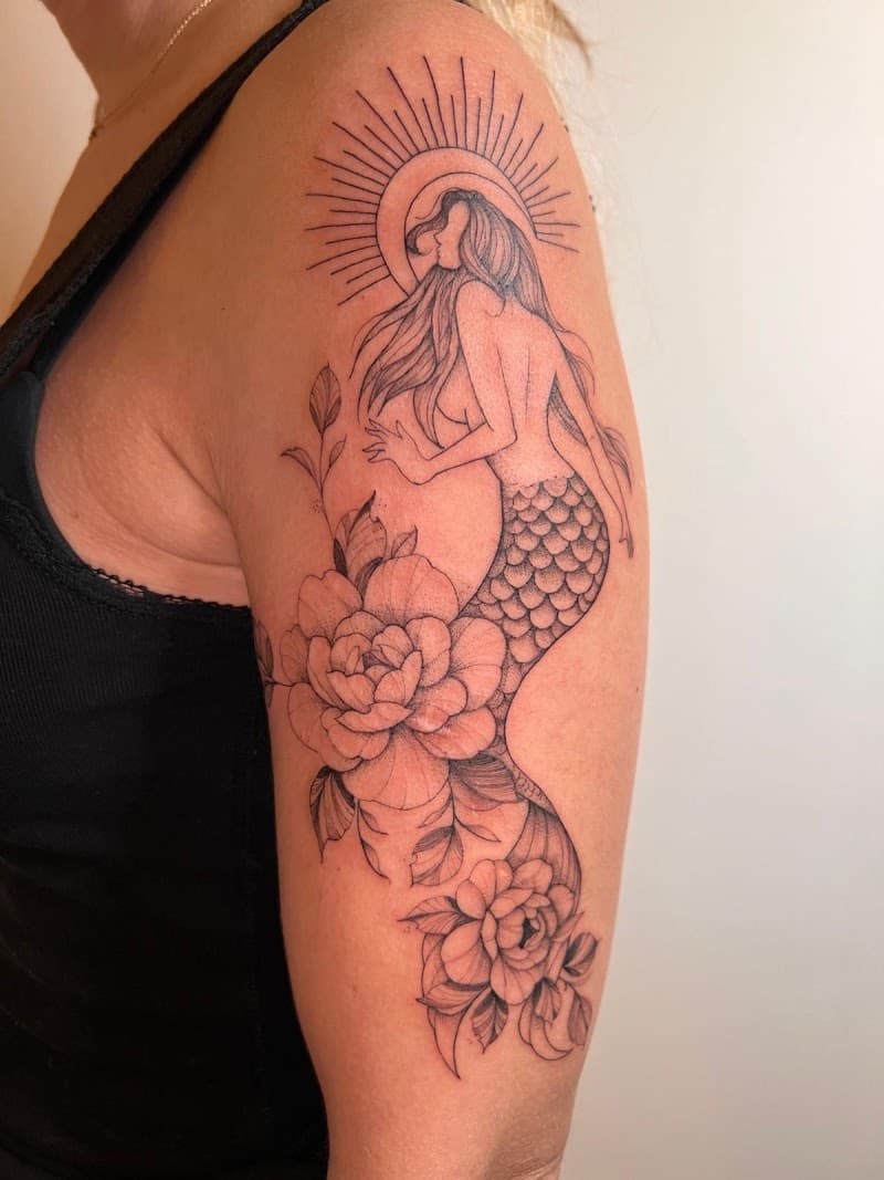 Fineline tattoo van een zeemeermin met bloemen en een zon op de bovenarm.