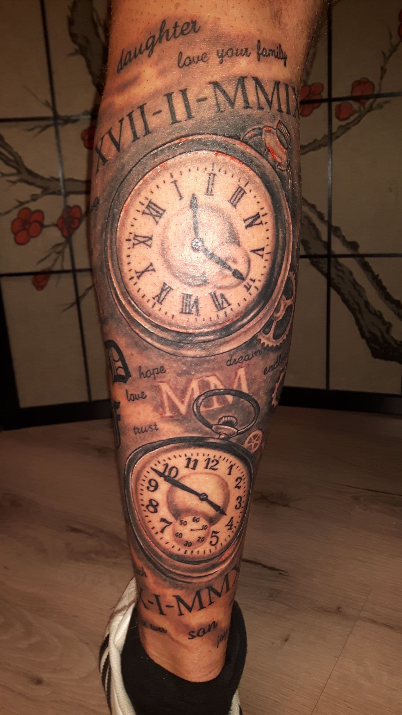 Realistische tattoo van twee zakhorloges, Romeinse cijfers en tekst op onderbeen.