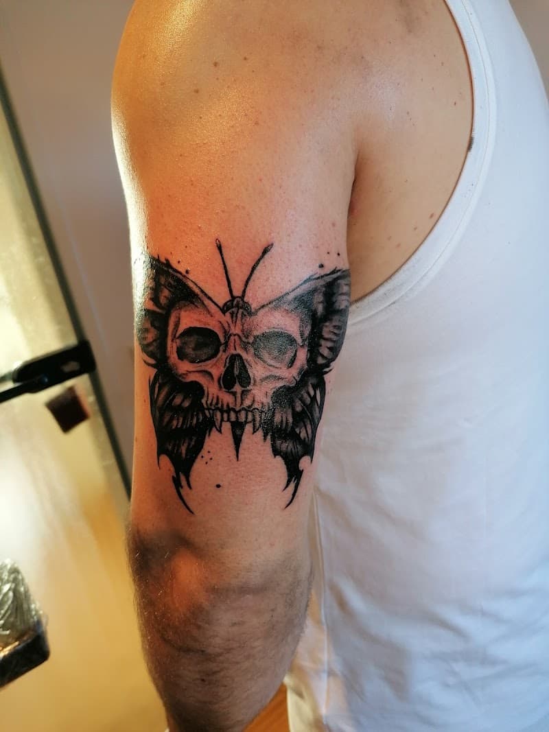 Zwart-wit tattoo van een vlinder met een doodskop in de vleugels op de bovenarm.