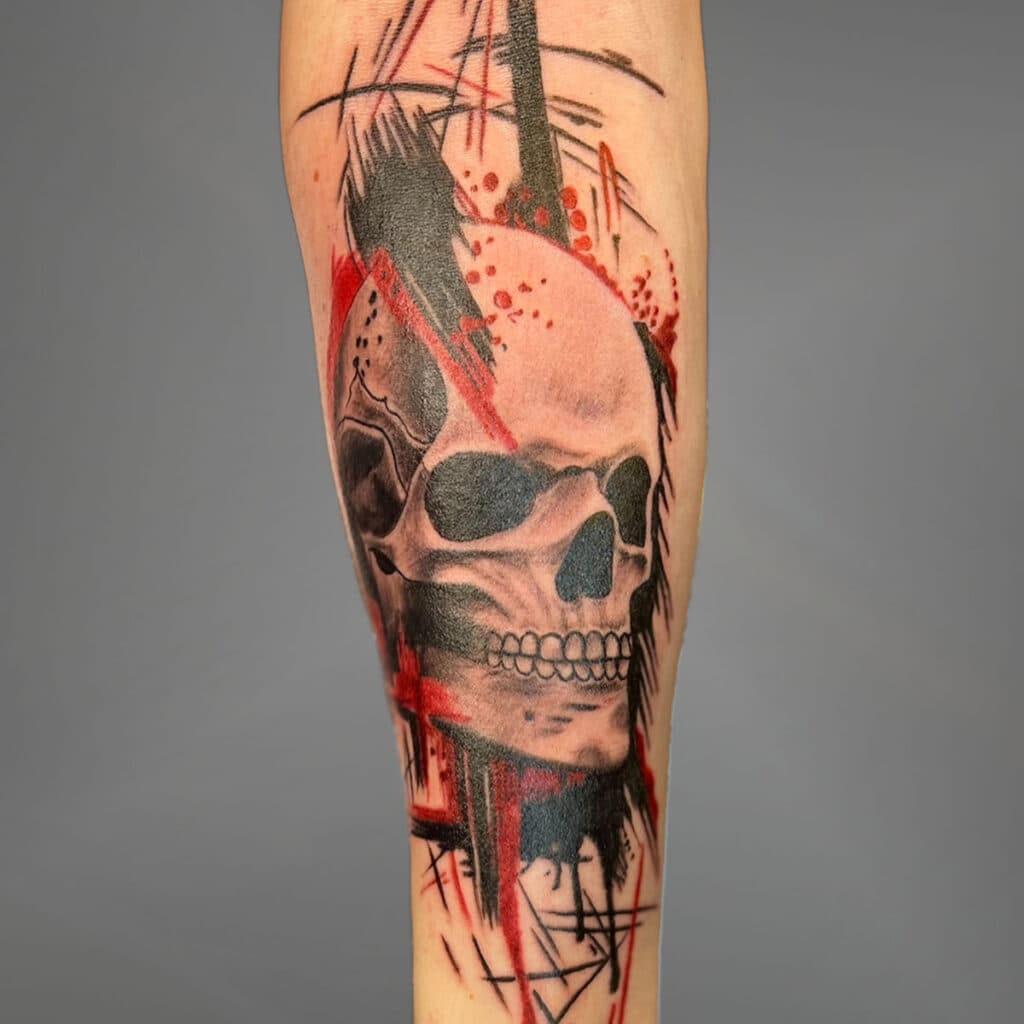 Schedel tattoo met abstracte rode en zwarte penseelstreken op de onderarm.
