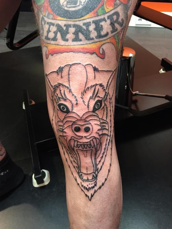 Lijntekening van een grommende wolfskop op het onderbeen.