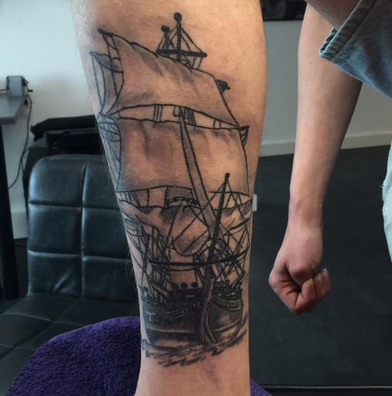 Zwart-wit schets tattoo van een zeilschip op het onderbeen.