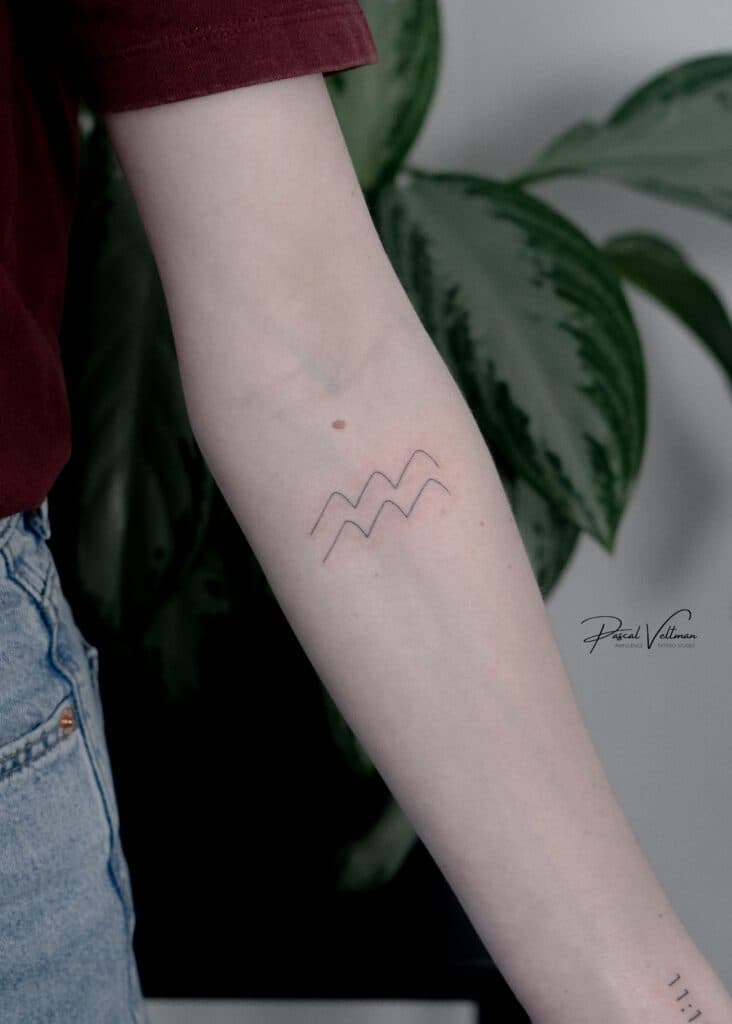 Minimalistische fineline tattoo van golven en '11:11' op onderarm.