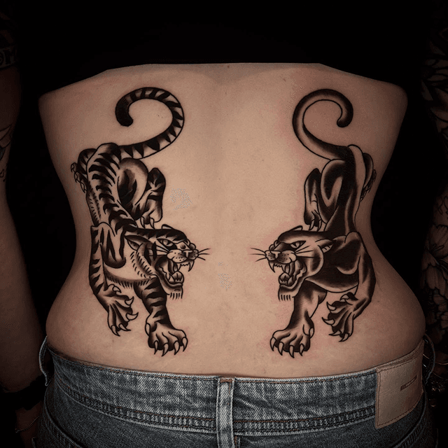 Twee traditionele tattoos van een tijger en een panter op de onderrug.