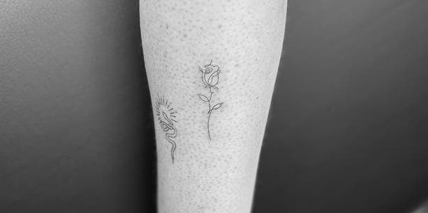 Fineline tattoos van een slang en een roos op de onderarm.