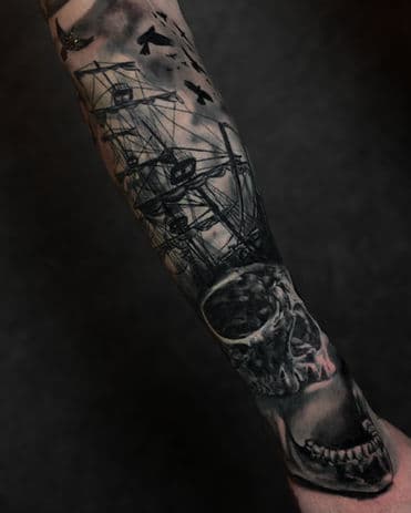 Gedetailleerde blackwork tattoo van een schedel, zeilschip en vogels op de onderarm.