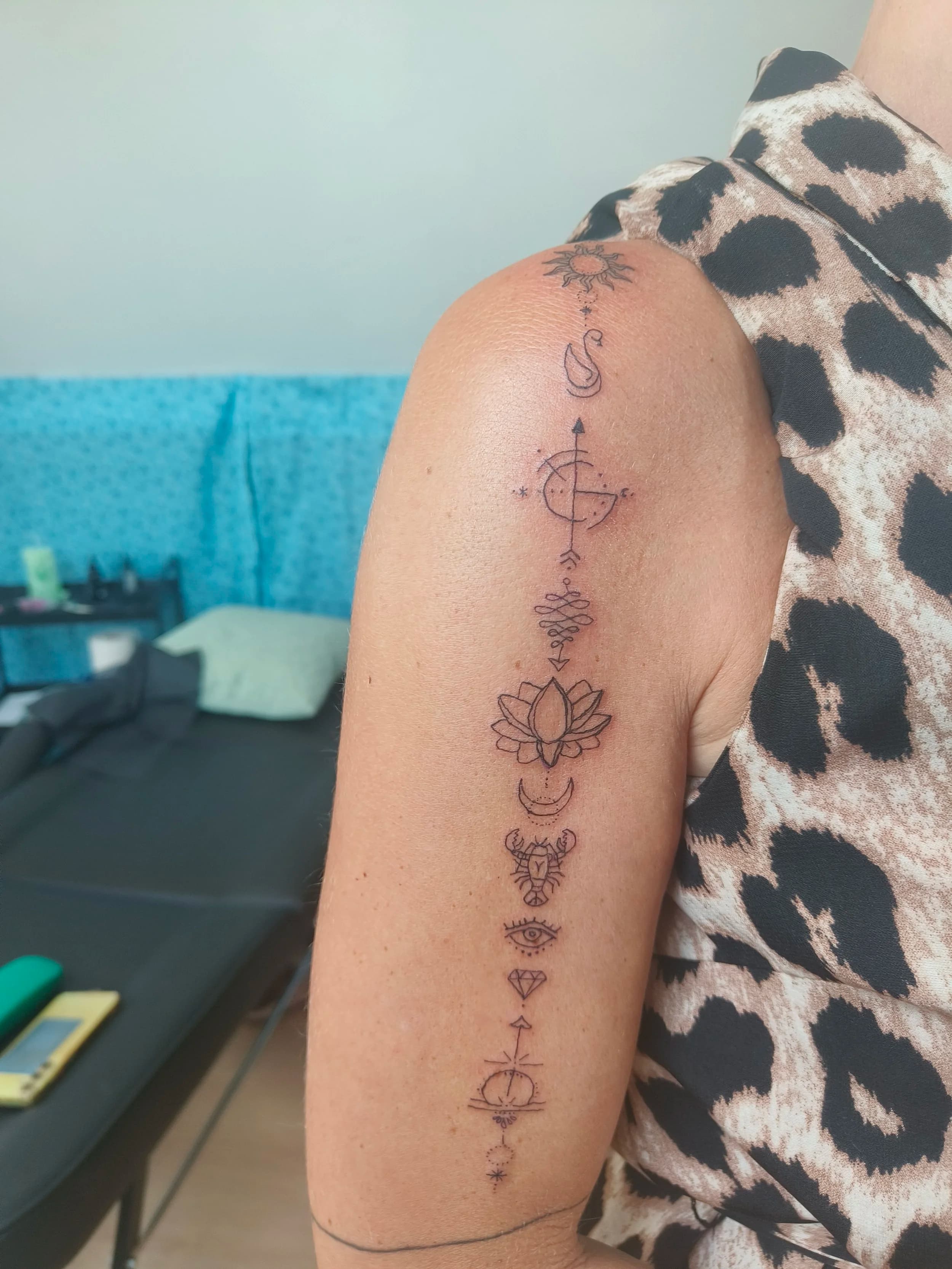 Fineline tattoo met een reeks symbolen op de bovenarm.