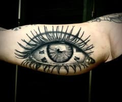 Realistisch oog met een klok erin verwerkt op de binnenkant van de bovenarm.