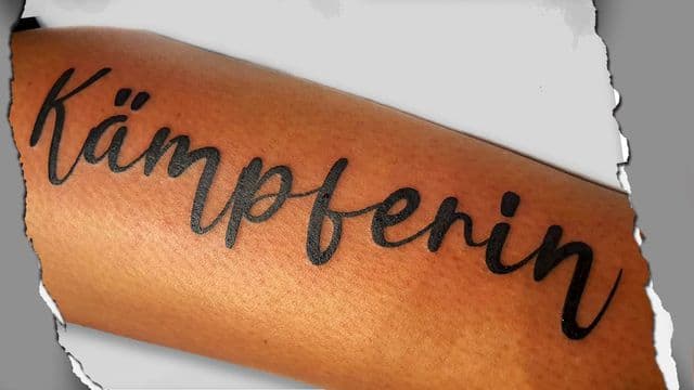 Zwart 'Kämpferin' woord in sierlijk handschrift op onderarm.