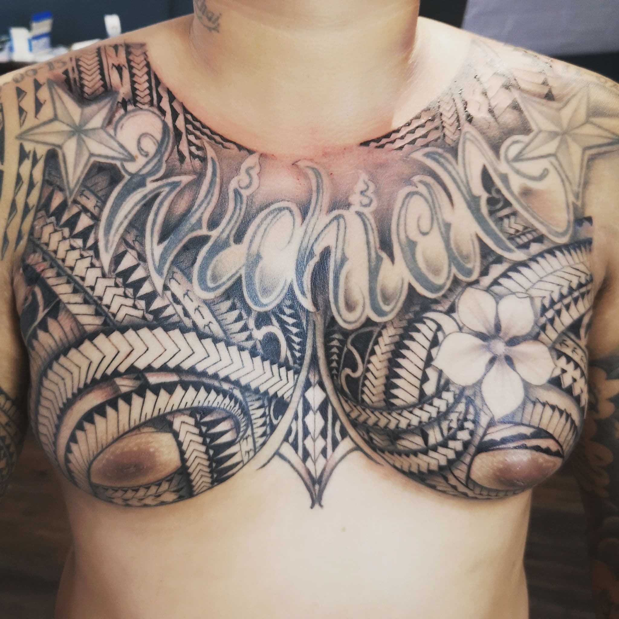 Grote Polynesische borsttattoo met scriptnaam en bloem.