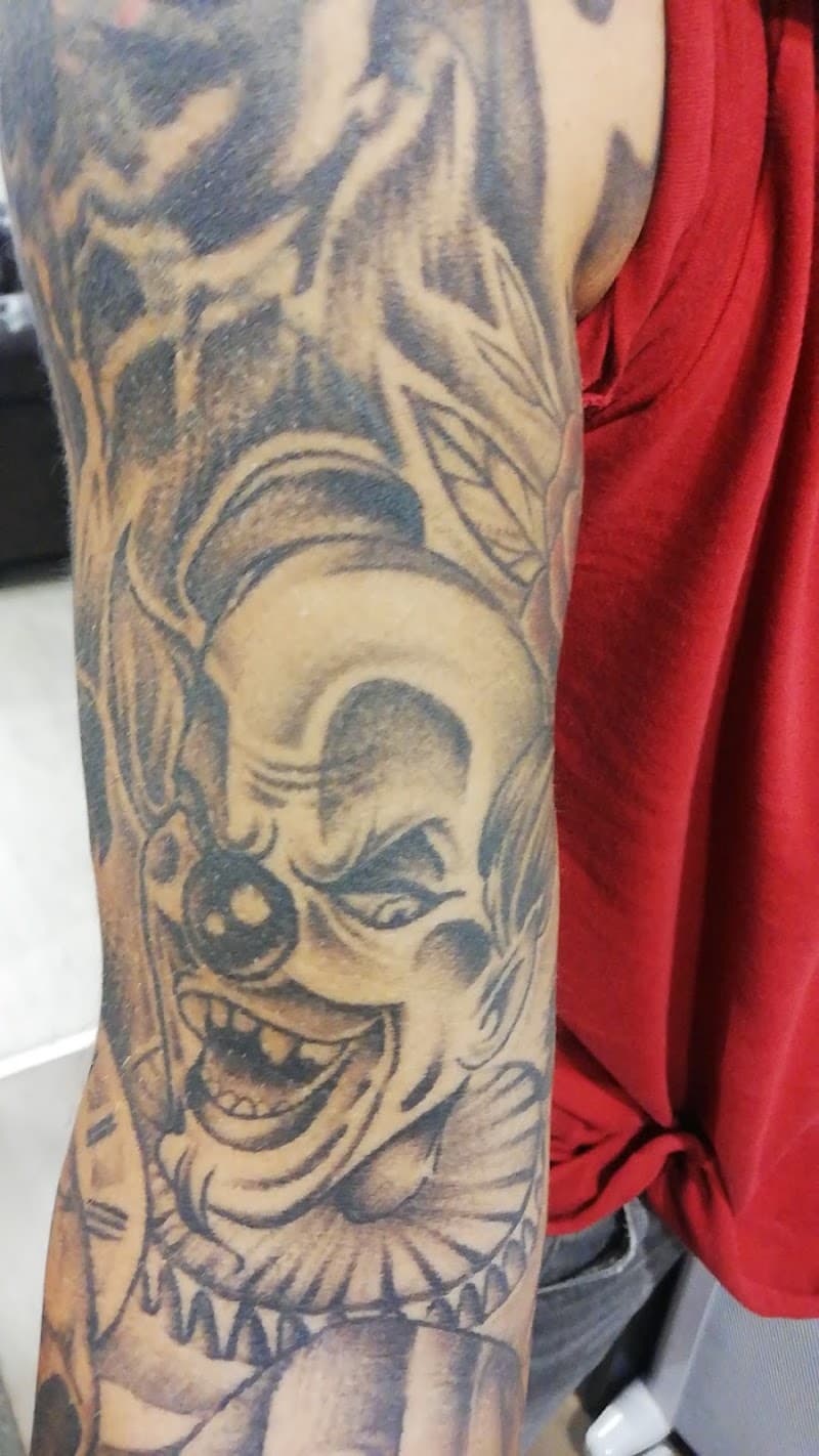 Zwart-wit tattoo van een lachende boze clown op de bovenarm.