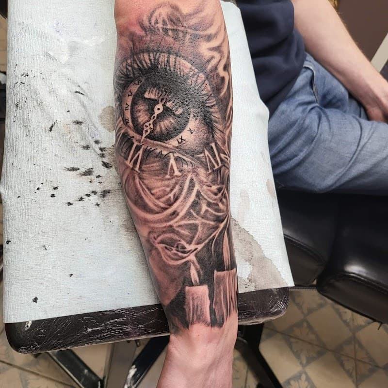 Zwart-wit tattoo van een oog met klok en kaarsen op de onderarm.