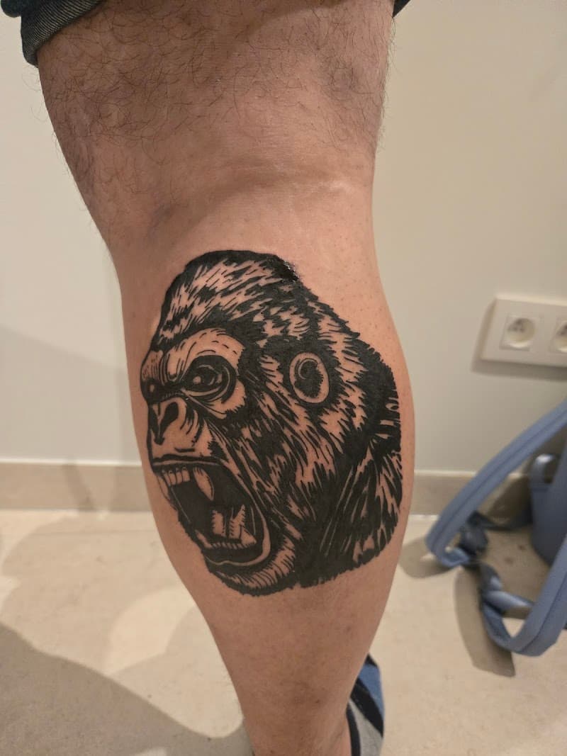 Zwart-wit blackwork tattoo van een brullende gorilla kop op een kuit.