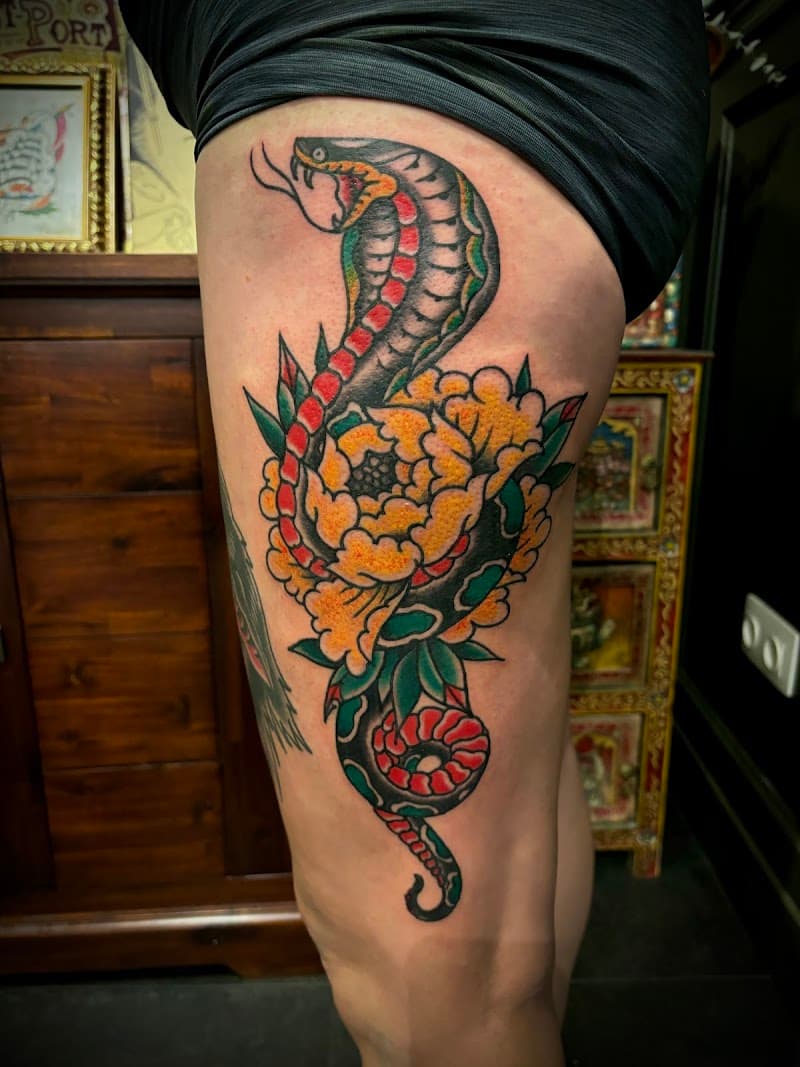 Traditionele tattoo van een cobra en een gele pioenroos op het bovenbeen.