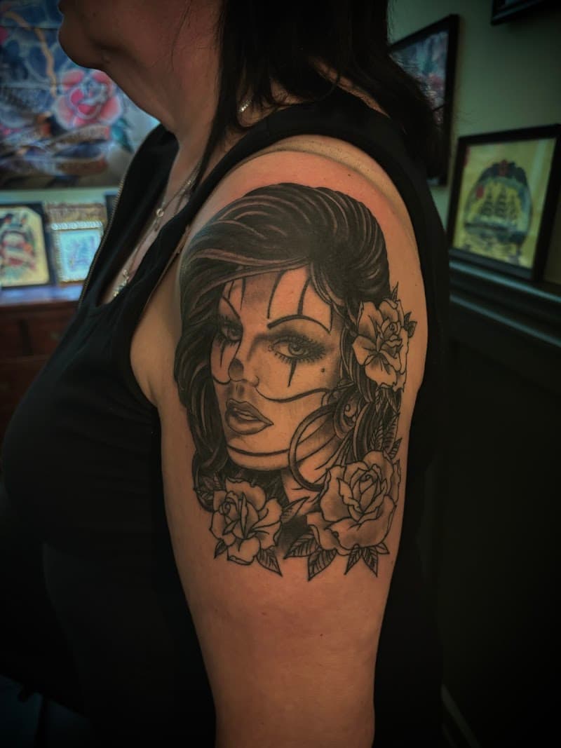 Zwart-wit portret van een vrouw met clownsmake-up en rozen op de bovenarm.