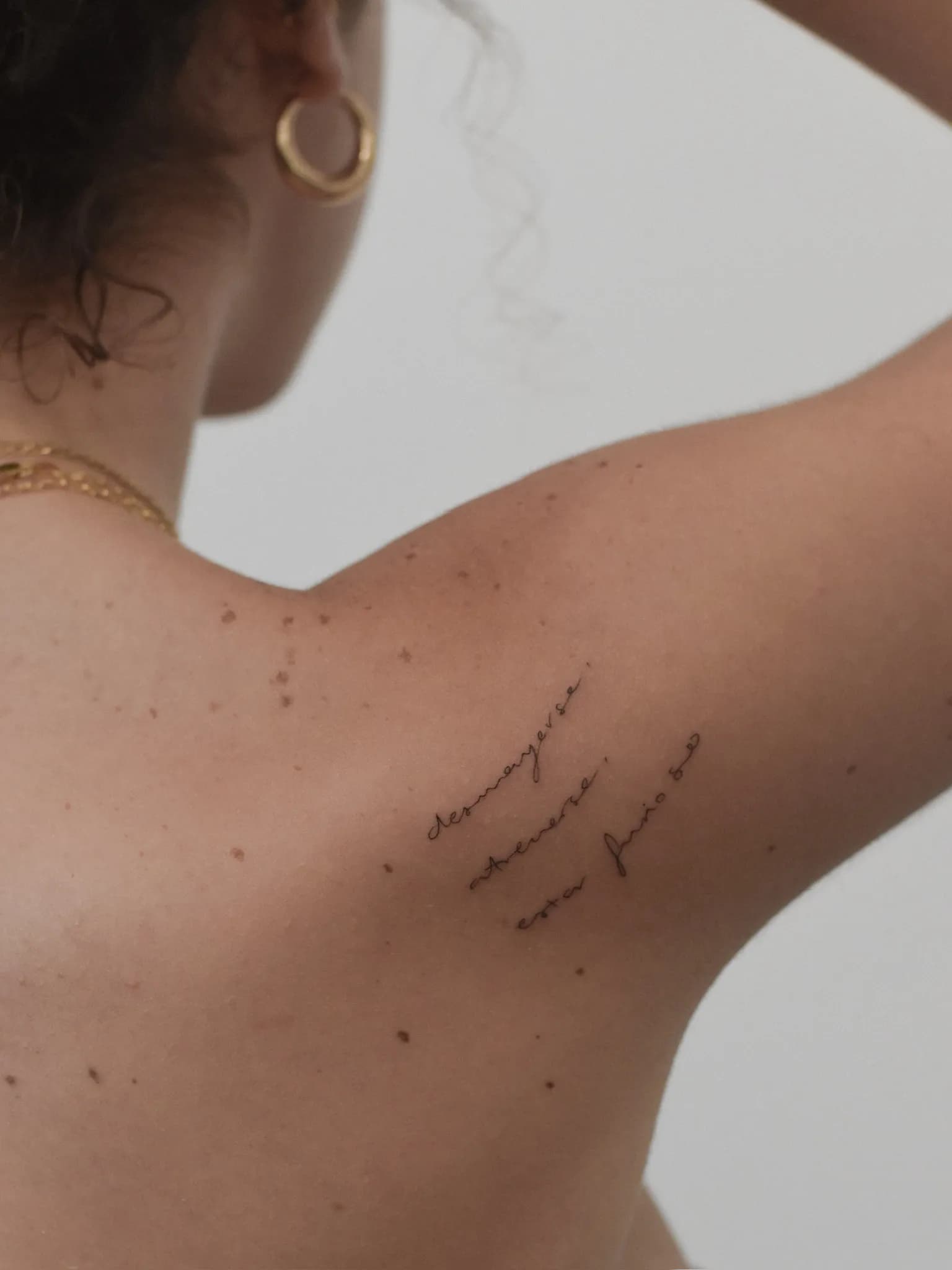 Fineline tekst tattoo in sierlijk handschrift op het schouderblad.