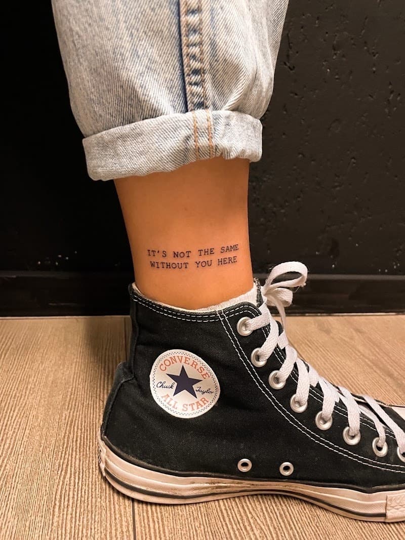 Minimalistische tekst tattoo 'IT'S NOT THE SAME WITHOUT YOU HERE' op enkel.