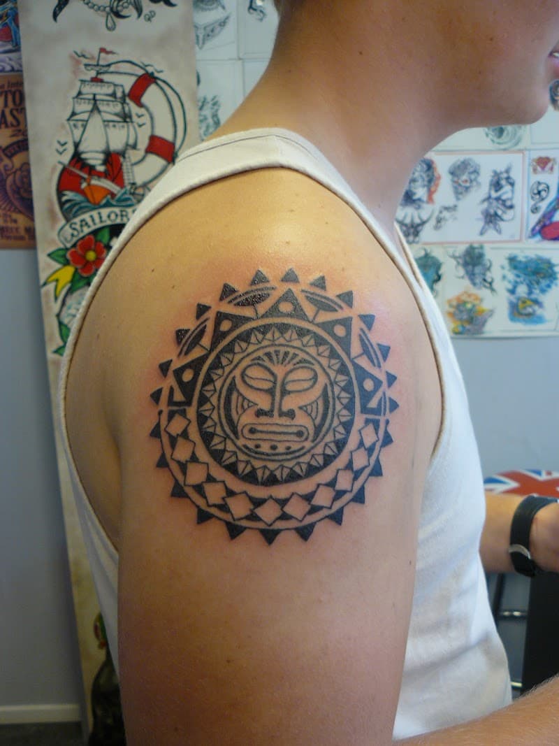 Polynesische zon tattoo met tiki gezicht op bovenarm.