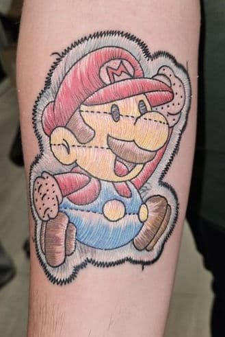 Mario tattoo in de stijl van een geborduurde patch op de onderarm.