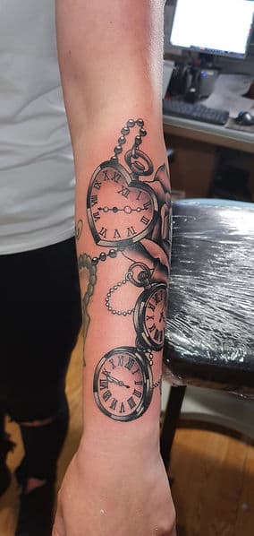 Zwart-wit tattoo van drie zakhorloges en een roos op de onderarm.