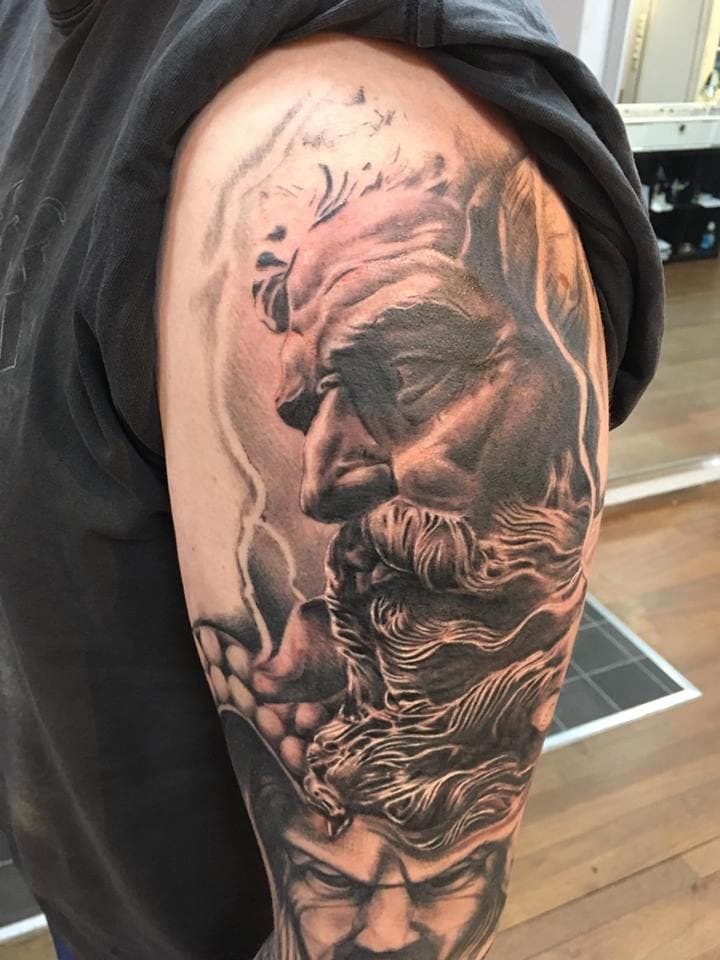 Realistische zwart-wit tattoo van een Griekse god (Zeus of Poseidon) op de bovenarm.