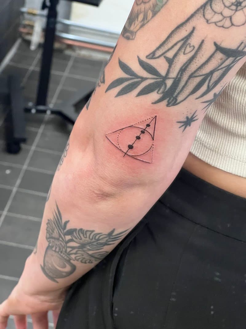 Fineline tattoo van het Relieken van de Dood symbool op de elleboog.