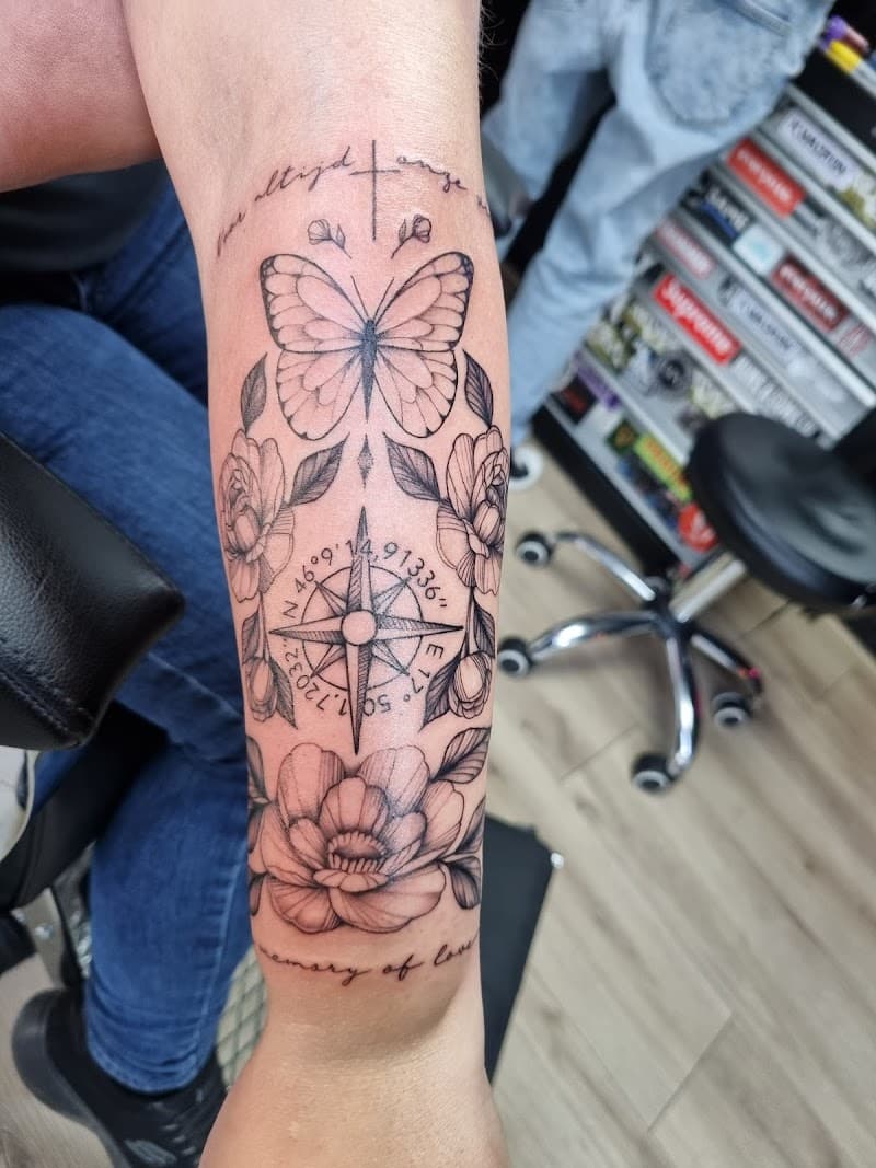 Fineline half-sleeve met vlinder, kompas, bloemen en tekst op onderarm.