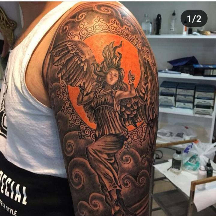 Grote zwart-wit tattoo van een engel in een sierlijke cirkel op de bovenarm.