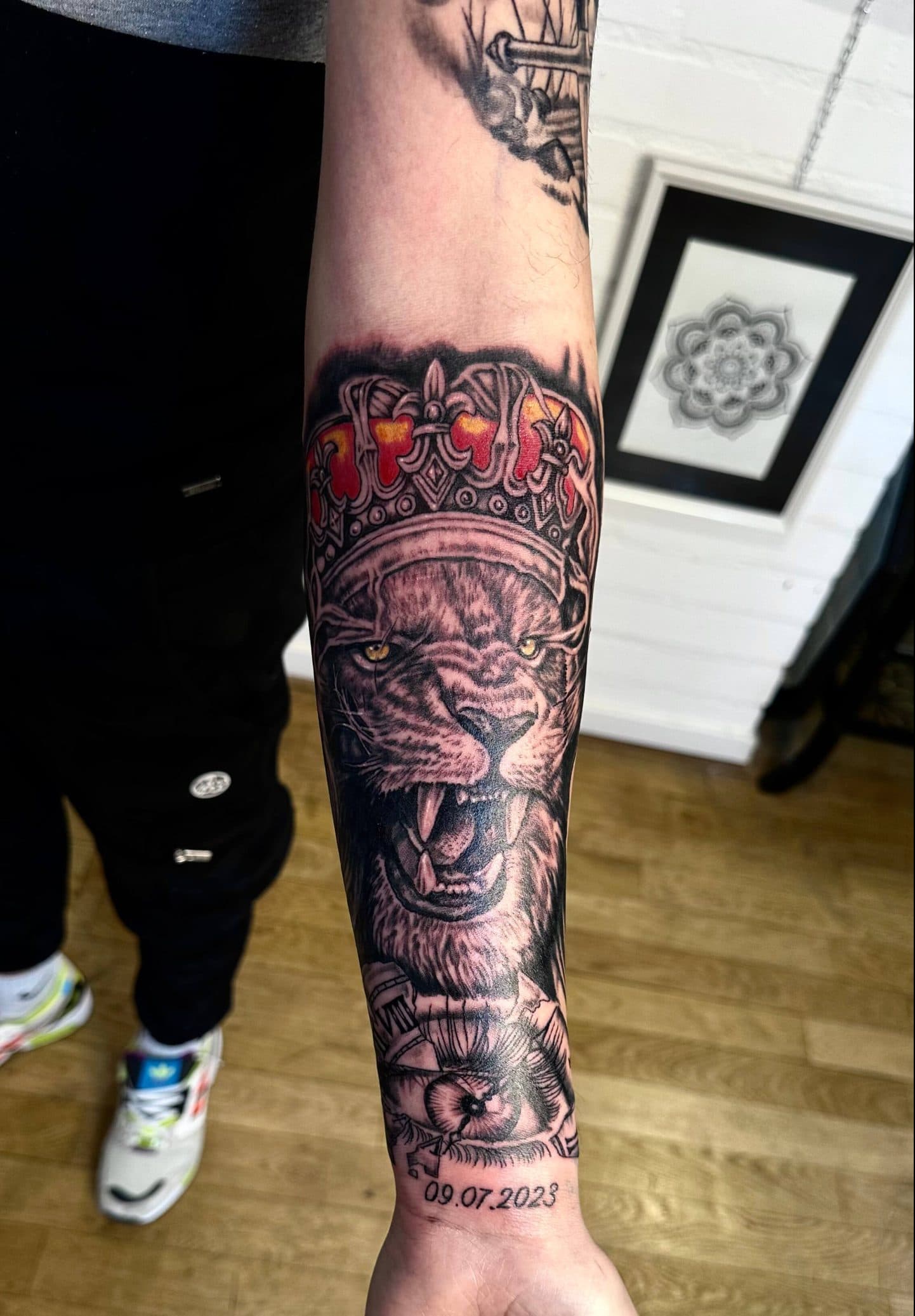 Realistische leeuw met kroon, oog en datum op onderarm.