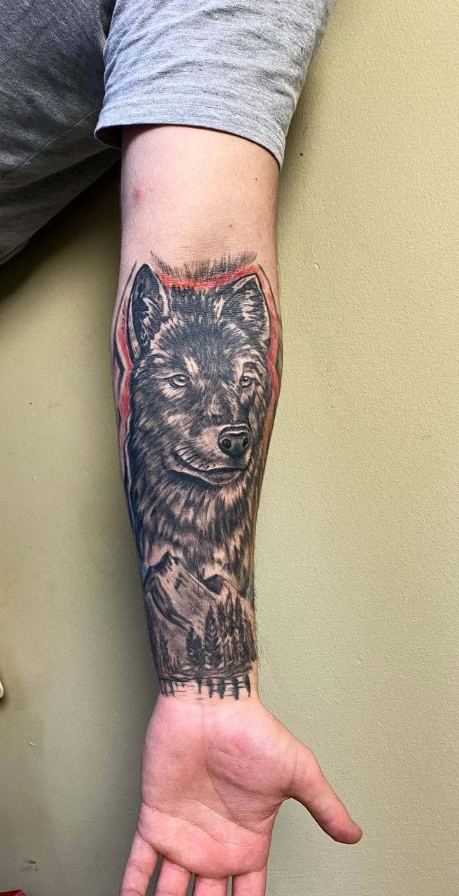 Realistische wolfskop met bergen en bomen op de onderarm.