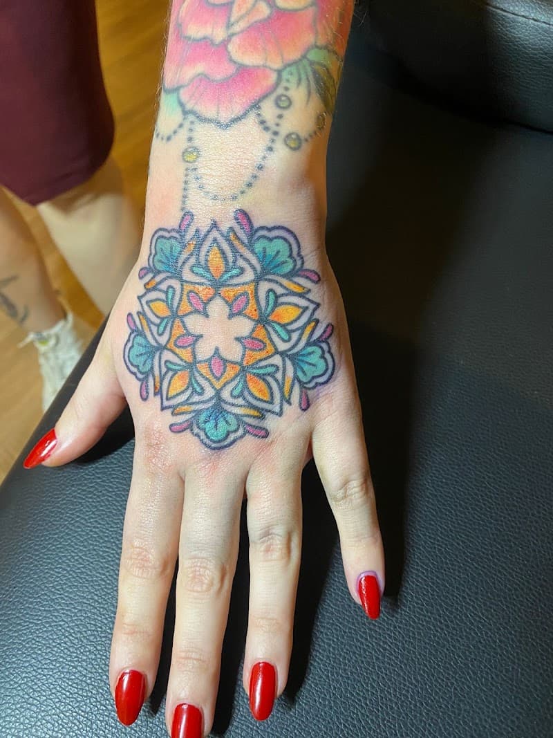 Kleurrijke mandala tattoo op de bovenkant van een hand.