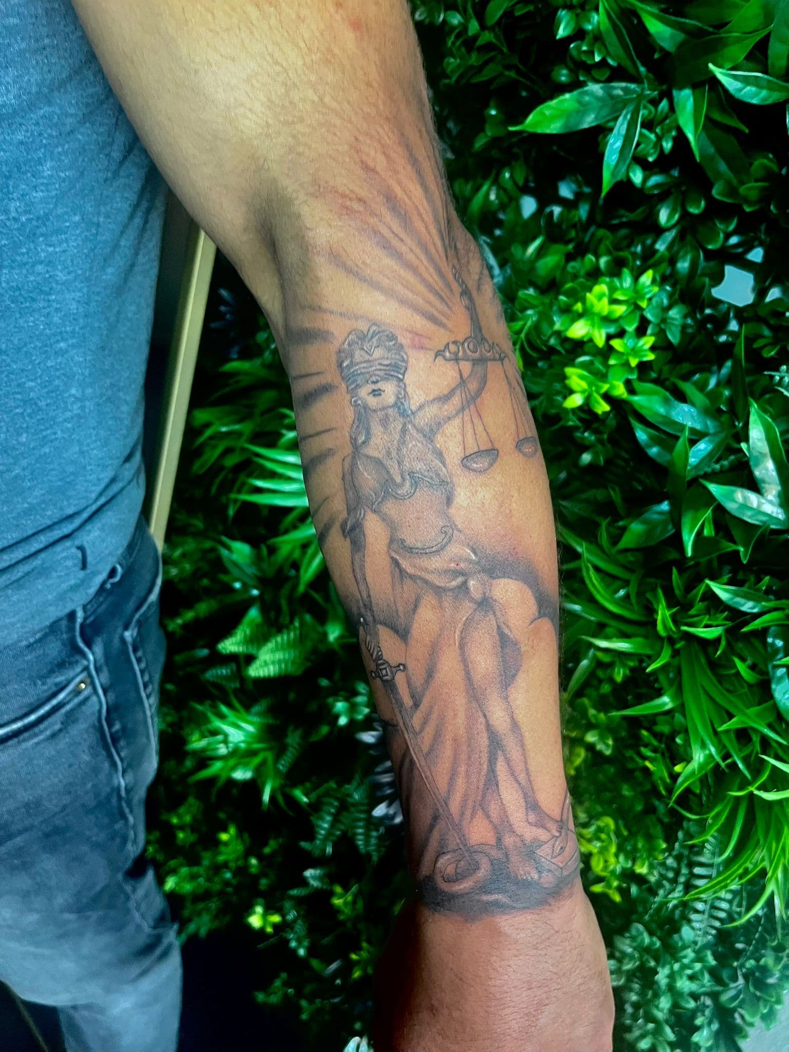 Zwart-wit tattoo van Vrouwe Justitia op de onderarm.