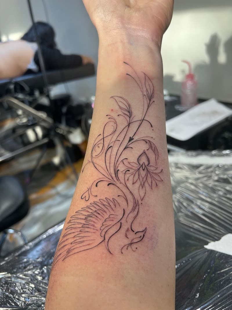 Fineline feniks met bloemen en sierlijke lijnen op onderarm.