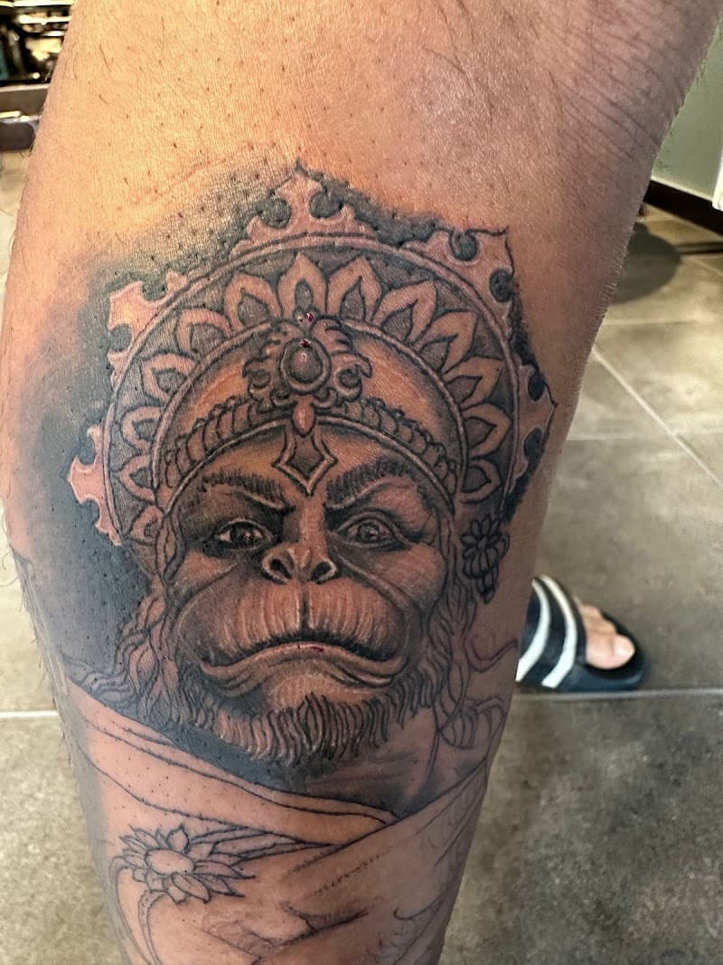 Zwart-wit tattoo van de hindoegod Hanuman met een kroon op het onderbeen.