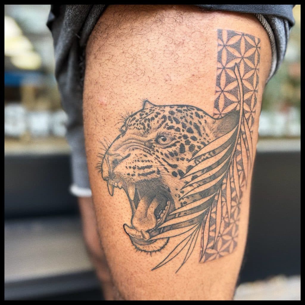 Brullende jaguar met palmblad en geometrisch patroon op bovenbeen.